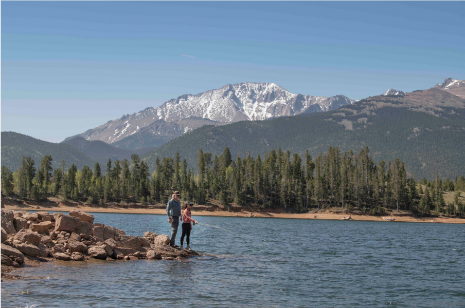 Gallery 1 - Two people fly fishing at a lake at the base of a mountain.