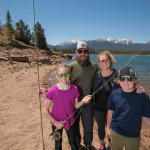 Gallery 4 - A family standing in front of a lake and mountain with fishing poles.