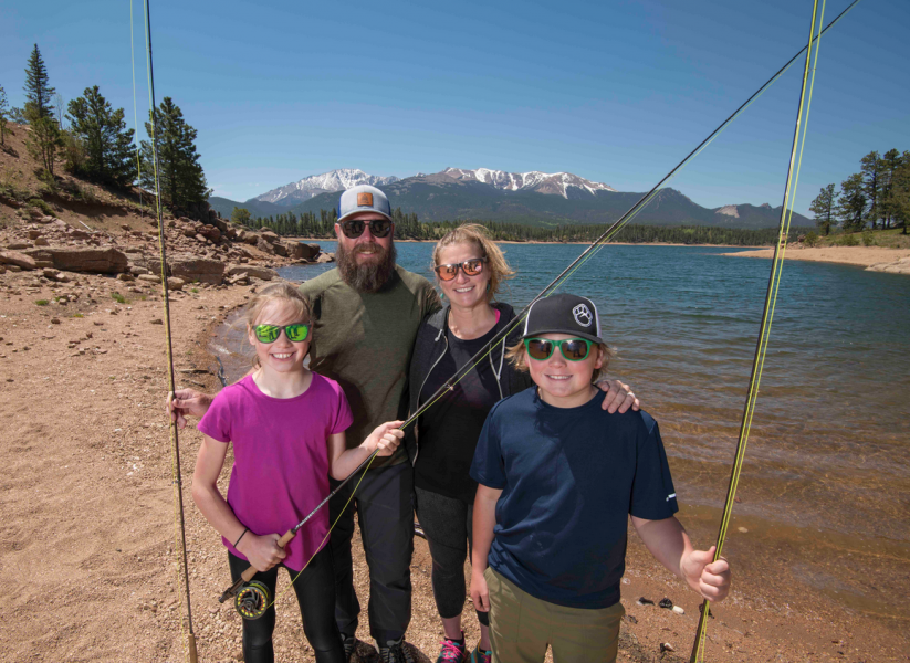 Gallery 4 - A family standing in front of a lake and mountain with fishing poles.